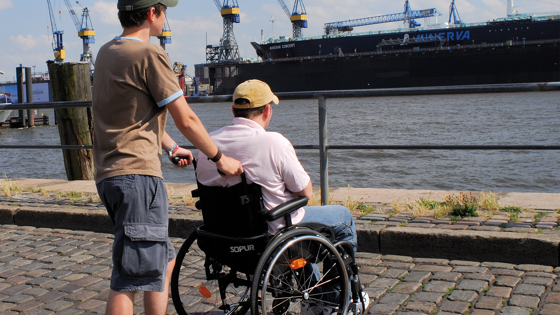 Ein Rollstuhlfahrer mit seiner Begleitperson am Hamburger Hafen