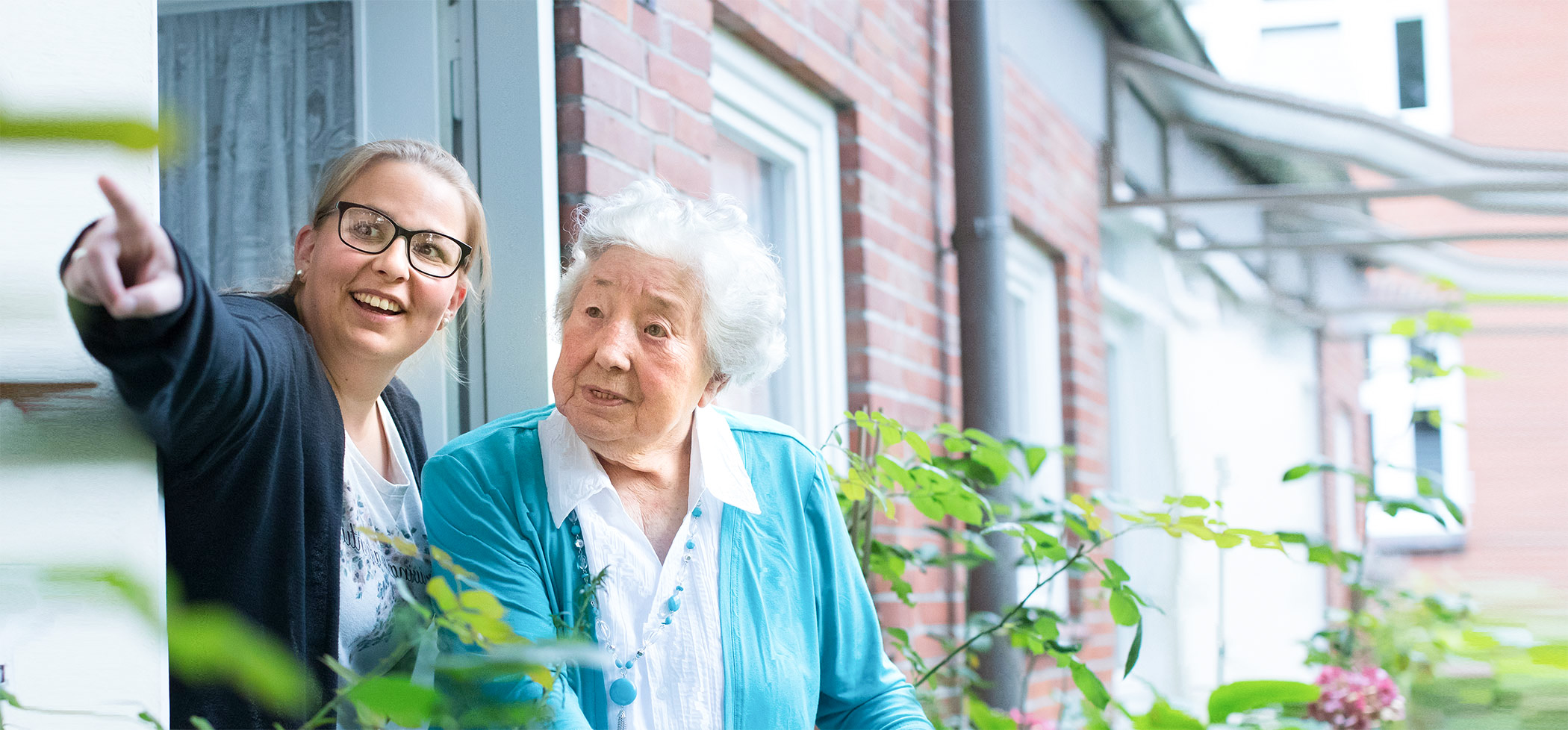 Ältere Frau sitzt in ihrem Garten und lächelt in die Kamera