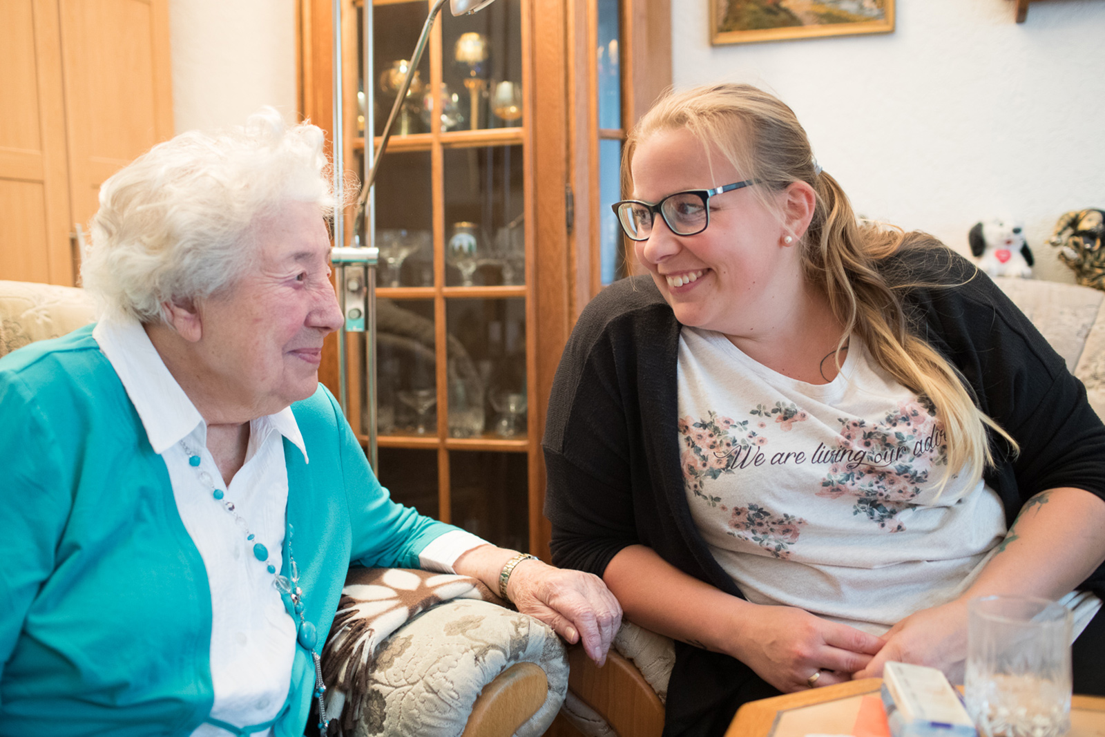 Ältere Frau und Ihre Pflegerin schauen sich grinsend an