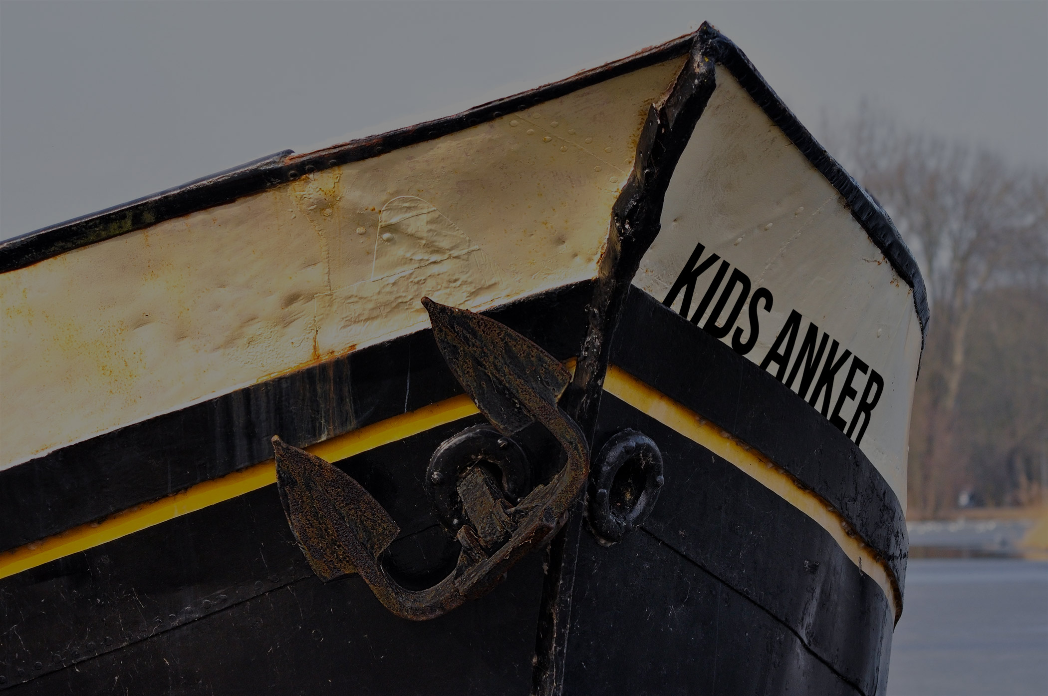 Der Bug eines Schiffes ist zu sehen, an dem ein Anker hängt. Auf dem Boot steht „Kids Anker“